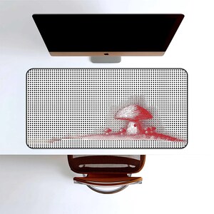May include: A rectangular desk mat with a black and white dotted pattern and a red mushroom illustration. The mat is on a white desk, with a computer monitor above and a brown chair below.