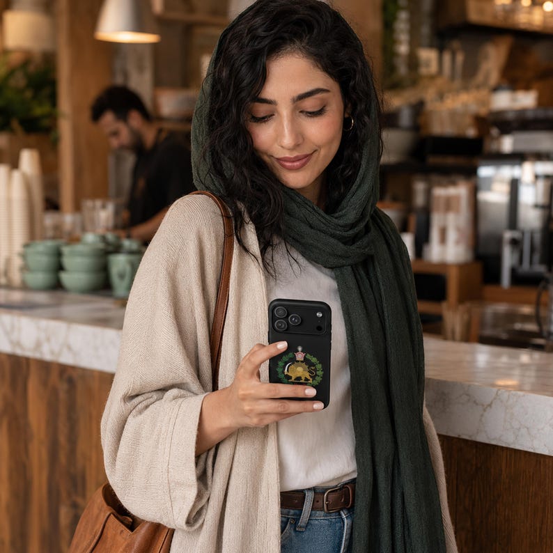 Puede incluir: Una funda de smartphone negra con un emblema circular que muestra un le&oacute;n dorado, una corona y hojas de laurel verdes. La funda tiene un m&oacute;dulo de c&aacute;mara prominente con tres lentes. El dispositivo se sostiene en la mano, mostrando el dise&ntilde;o.