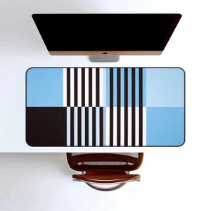 May include: A rectangular desk mat with a geometric design in shades of blue, black, and white. The pattern includes vertical stripes and solid color blocks. A computer monitor sits above the mat, and a brown chair is positioned below.
