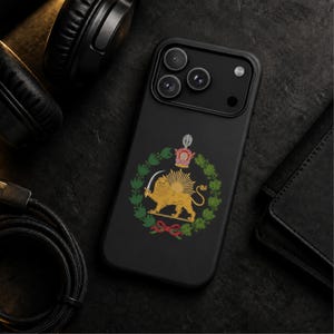 Puede incluir: Una funda de smartphone en negro mate con un emblema central del Le&oacute;n y el Sol. El dise&ntilde;o muestra un le&oacute;n dorado sosteniendo una espada frente a un sol naciente, rodeado por una corona de laurel verde y rematado con una corona real.