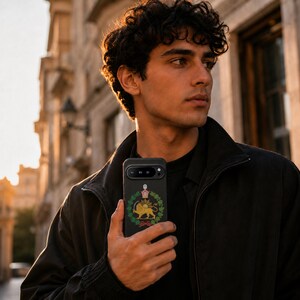 Puede incluir: Una funda de smartphone negra con un emblema central de un le&oacute;n dorado sosteniendo una espada, rodeado por una corona de laurel verde y rematado con una corona. La funda tiene una barra de c&aacute;mara horizontal y un acabado negro mate liso.