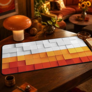 May include: A rectangular desk mat featuring a repeating pattern of three-dimensional square tiles arranged in horizontal rows. The top section consists of white tiles, the middle section of yellow-orange tiles, and the bottom section of red tiles.