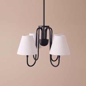 May include: A matte black metal chandelier featuring four curved arms extending from a central stem. Each arm supports a white, tapered fabric lampshade. The fixture is suspended by a single vertical rod, creating a symmetrical lighting design.