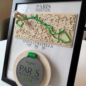 May include: A framed display featuring a 3D map of the Paris Marathon route with a green path, the text PARIS MARATHON, ELENA CURATELLA, 42,195 KM, PARIS FRANCE 2026 APR 12, and a silver medal with a green ribbon and the text Schneider Electric PARIS MARATHON 2026 12 AVRIL 2026.