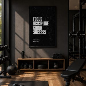 Può includere: Una stampa da parete rettangolare nera con testo bianco che recita FOCUS DISCIPLINE GRIND SUCCESS e THE FORMULA NEVER LIES. La stampa presenta una sottile trama marmorizzata ed è esposta in una sottile cornice nera su una parete grigia.