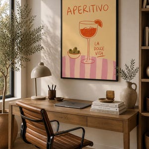 Könnte beinhalten: Ein gerahmter Kunstdruck mit gelbem Hintergrund, dem Text APERITIVO oben und LA DOLCE VITA an der Seite. Die Illustration zeigt ein Stielglas mit einer Orangenscheibe und Eiswürfeln sowie eine kleine Schale mit grünen Oliven.
