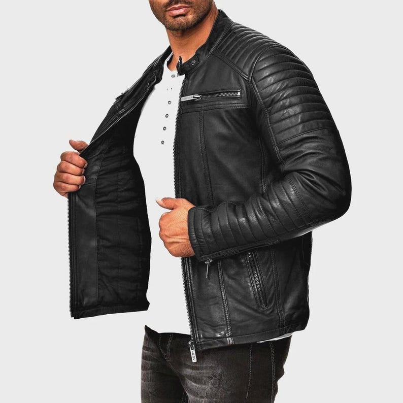 May include: Black leather jacket with a quilted design on the shoulders and upper arms. The jacket has a zipper closure, multiple pockets, and a stand-up collar. The model is wearing a white shirt underneath.