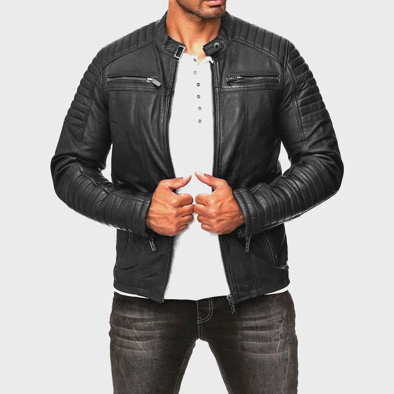 May include: Black leather jacket with a quilted design on the shoulders and sleeves. The jacket has a stand-up collar, zippered pockets, and a front zipper closure. The model is wearing a white shirt and dark jeans.
