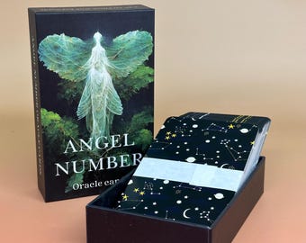 May include: A black box set of "Angel Number" oracle cards. The box features an illustration of an angel with leaf-like wings. The open box reveals a deck of cards with a black background and white constellation designs.