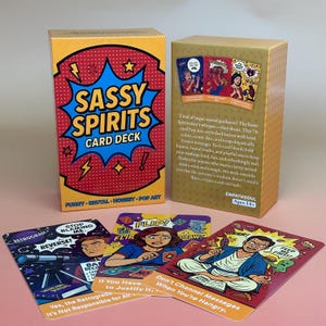 May include: A card deck titled "Sassy Spirits" with a red, yellow, and blue design. The box and cards feature Pop Art style illustrations and text. The deck includes cards with phrases like "Stop Blaming Me" and "Feed Me First!"