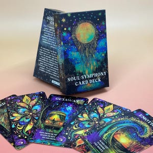 May include: A Soul Symphony Card Deck with a box featuring a celestial design with a large, glowing orb. The cards have colorful, artistic illustrations with phrases like "Getaway" and "In and out crashing like waves."