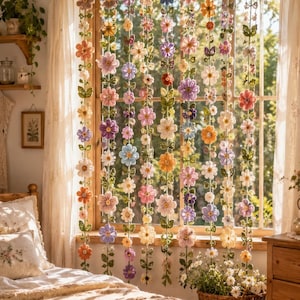 May include: A decorative window hanging featuring multiple vertical strands of crocheted flowers in various colors including pink, purple, orange, yellow, and white, interspersed with green crocheted leaves, suspended in front of a window.
