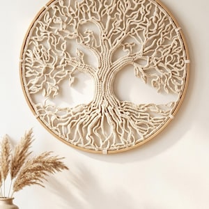 May include: A circular wall hanging featuring a cream-colored crocheted tree of life design mounted within a light-toned wooden hoop. The intricate fiber art displays a central trunk with sprawling branches and roots, secured by cord loops.