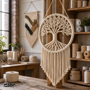 May include: A circular macrame wall hanging featuring an intricate tree of life design crafted from off-white cotton cord. The piece includes a dense canopy of knotted branches and a trunk that extends into long, straight fringe hanging downward.