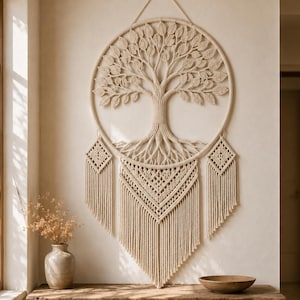 May include: A large circular macrame wall hanging featuring a central tree of life design with intricate leaf patterns and roots. The piece includes two smaller diamond-shaped accents on the sides and a long, layered fringe base in off-white cord.