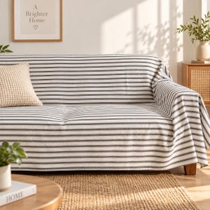 May include: A sofa covered in a fabric featuring horizontal dark gray and white stripes. A textured, cream-colored square throw pillow rests on the left side of the sofa. The fabric drapes over the arms and seat, providing full coverage.