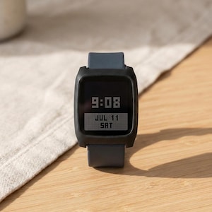 May include: A digital wristwatch with a matte black square case and a dark gray silicone strap. The screen displays the time 9:08 in a pixelated font, with the date JUL 11 and the day SAT shown in a rectangular box below the time digits.