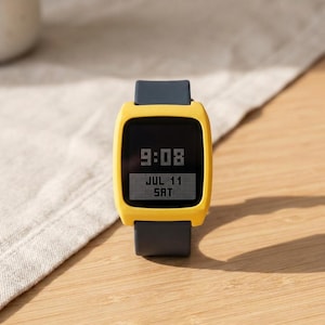 May include: A digital watch with a bright yellow square frame and a dark gray silicone strap. The black screen displays the time 9:08 in a pixelated font, with the date JUL 11 and the day SAT shown in a white rectangular box below the time.