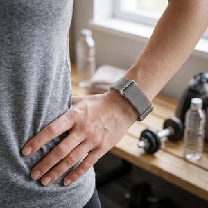 Könnte beinhalten: Eine silberfarbene Smartwatch mit einem feinen Metall-Mesh-Armband am Handgelenk. Die Uhr verfügt über ein rechteckiges Zifferblatt mit metallischem Finish und einen sicheren Verschlussmechanismus, was ein elegantes und funktionales Design ergibt.