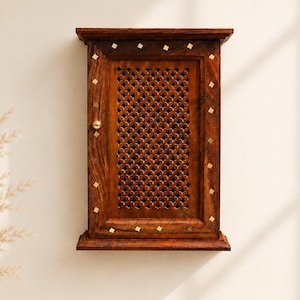 May include: A rectangular wall-mounted wooden cabinet with a dark brown finish. The front door features a central lattice panel with a repeating geometric cutout pattern and a small round brass knob. Small square brass inlays decorate the frame.