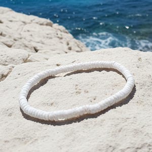 May include: A circular bracelet composed of numerous small, flat, white disc-shaped beads strung together in a continuous loop. The beads have a matte texture and are uniform in size, creating a simple, flexible band that rests in a circular shape.