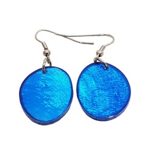 Könnte beinhalten: Ein Paar blaue Ohrringe mit glänzender, strukturierter Oberfläche. Die Ohrringe sind oval und hängen an silberfarbenen Fischhaken-Ohrdrähten. Die Ohrringe haben eine leuchtend blaue Farbe.