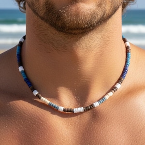 May include: A beaded necklace featuring a repeating pattern of small, cylindrical disc-shaped beads in shades of dark brown, white, light blue, and deep navy blue. The necklace sits closely around the neck, showcasing a uniform arrangement of these colourful, textured beads strung together in a continuous circular design.