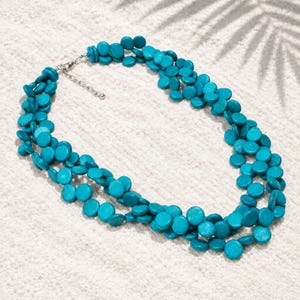Op de afbeelding: Een meerstrengs ketting bestaande uit talloze kleine, ronde, turquoise kralen. De ketting is voorzien van een zilverkleurige metalen verlengketting met een karabijnsluiting, waardoor de lengte rond de hals kan worden aangepast.