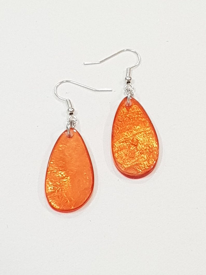 Op de afbeelding: Een paar oranje druppelvormige oorbellen met zilverkleurige oorhaken. De oorbellen hebben een getextureerde, iriserende afwerking en worden gepresenteerd tegen een witte achtergrond. Deze oorbellen zijn een stijlvol accessoire.