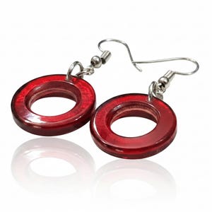 K&ouml;nnte beinhalten: Ein Paar rote, kreisf&ouml;rmige Ohrringe mit silberfarbenen Haken. Die Ohrringe haben eine gl&auml;nzende Oberfl&auml;che und spiegeln sich auf einer wei&szlig;en Oberfl&auml;che. Ein schlichtes, aber elegantes Accessoire.
