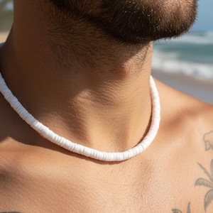 Könnte beinhalten: Eine weiße Perlenkette wird um den Hals getragen. Die Halskette besteht aus kleinen, runden, weißen Perlen. Der Hintergrund zeigt eine Strandszene mit Meer und Himmel.