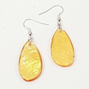 Op de afbeelding: Een paar druppelvormige oorbellen met een doorschijnende, amberkleurige uitstraling. De oorbellen hebben een getextureerd oppervlak en zijn bevestigd aan zilverkleurige oorhaakjes. De sieraden staan tegen een witte achtergrond. Ongeveer 2 cm lang.