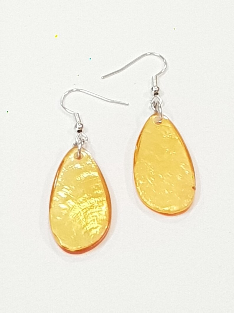 Op de afbeelding: Een paar druppelvormige oorbellen met een doorschijnende, amberkleurige uitstraling. De oorbellen hebben een getextureerd oppervlak en zijn bevestigd aan zilverkleurige oorhaakjes. De sieraden staan tegen een witte achtergrond. Ongeveer 2 cm lang.