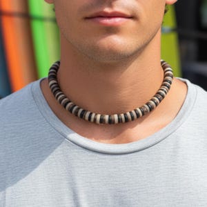 Könnte beinhalten: Eine Halskette mit abwechselnd dunkelbraunen, hellbraunen und weißen runden Perlen. Die Halskette wird um den Hals getragen. Die Halskette ist ein lässiges Accessoire aus natürlichen Materialien.