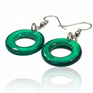 K&ouml;nnte beinhalten: Ein Paar gr&uuml;ne, kreisf&ouml;rmige Ohrringe mit silberfarbenen Haken. Die Ohrringe haben eine gl&auml;nzende Oberfl&auml;che und reflektieren das Licht. Das Design ist schlicht und modern. Jeder Ohrring hat einen Durchmesser von ca. 2,5 cm.