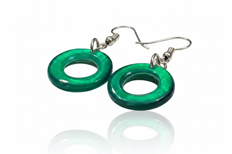 K&ouml;nnte beinhalten: Ein Paar gr&uuml;ne, kreisf&ouml;rmige Ohrringe mit silberfarbenen Haken. Die Ohrringe haben eine gl&auml;nzende Oberfl&auml;che und reflektieren das Licht. Das Design ist schlicht und modern. Jeder Ohrring hat einen Durchmesser von ca. 2,5 cm.