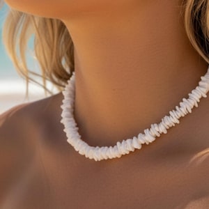 Puede incluir: Collar de conchas blancas con un diseño natural y orgánico. El collar está hecho de pequeñas conchas blancas de forma irregular ensartadas. La joya se lleva alrededor del cuello.