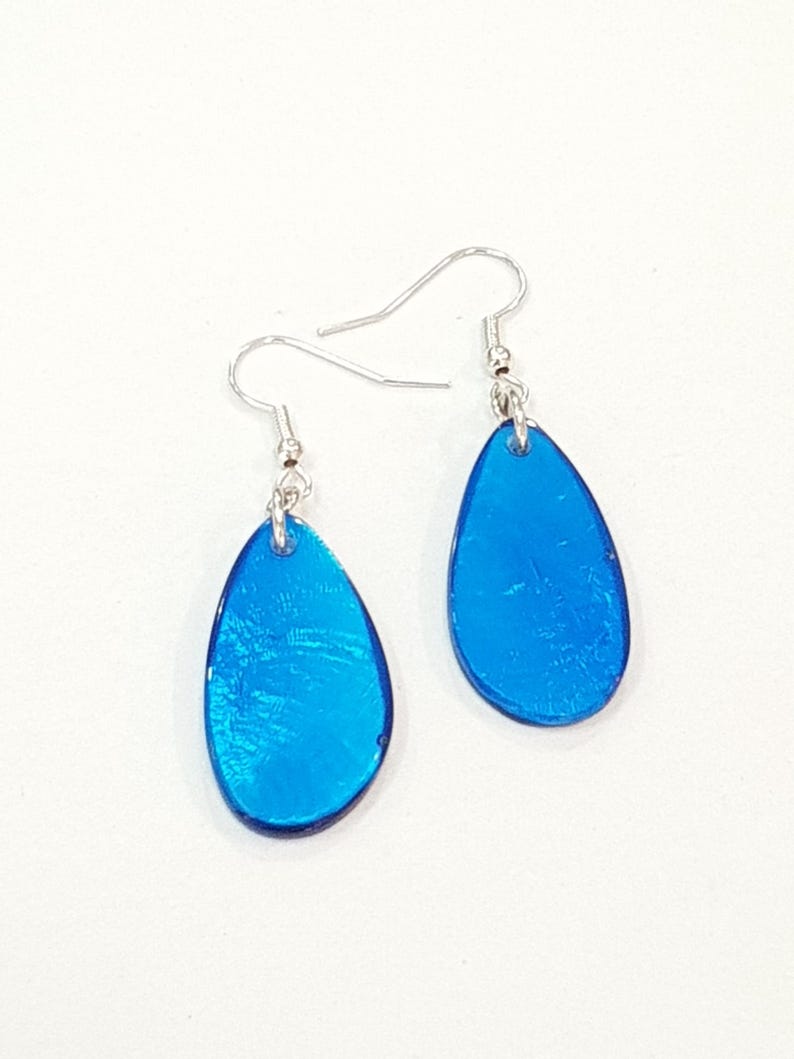 Op de afbeelding: Een paar helderblauwe druppelvormige oorbellen met zilverkleurige haken. De oorbellen hebben een glanzende afwerking en reflecteren het licht. Ze worden gepresenteerd tegen een witte achtergrond.