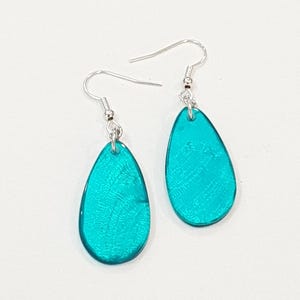 Op de afbeelding: Een paar turquoise teardrop oorbellen met zilverkleurige oorhaken. De oorbellen hebben een getextureerde, iriserende afwerking die licht reflecteert. De oorbellen worden gepresenteerd tegen een witte achtergrond.