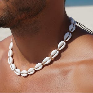 Könnte beinhalten: Halskette aus weißen Muscheln an einer schwarzen Kordel. Die ovalen Muscheln sind aufgereiht und bilden eine Kette. Der Stil ist natürlich und erinnert an den Strand.