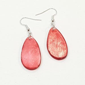 Op de afbeelding: Een paar rode druppelvormige oorbellen met zilverkleurige oorhaken. De oorbellen hebben een getextureerd oppervlak en een glanzende afwerking. De oorbellen zijn een eenvoudig, elegant accessoire.