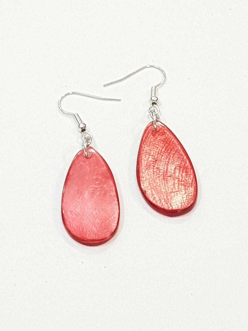 Op de afbeelding: Een paar rode druppelvormige oorbellen met zilverkleurige oorhaken. De oorbellen hebben een getextureerd oppervlak en een glanzende afwerking. De oorbellen zijn een eenvoudig, elegant accessoire.