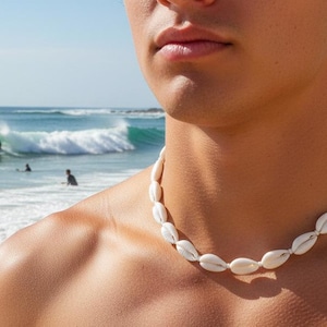 Könnte beinhalten: Eine Halskette aus weißen Muscheln wird um den Hals getragen. Die Kette besteht aus mehreren weißen Muscheln, die aneinandergereiht sind. Der Hintergrund zeigt einen Strand mit Wellen und Surfern.