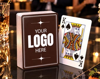 May include: A deck of playing cards with a dark brown back featuring the white text YOUR LOGO HERE and star accents, displayed next to a single King of Spades playing card with a traditional crown, sword, and spade suit symbol illustration.