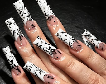 Uña postiza personalizada, estampado floral negro sobre base blanca con tachuelas plateadas, diseño de contraste llamativo, uñas de boda vanguardistas para la novia moderna.