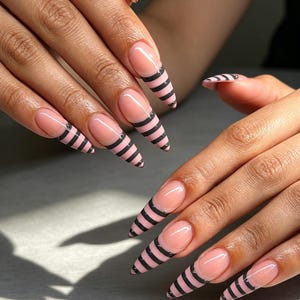 Può includere: Unghie lunghe a forma di mandorla con una base color nude e strisce orizzontali nere sulle punte. Il design imita lo stile di una manicure francese, con il motivo a righe concentrato sulla parte estesa di ogni unghia.
