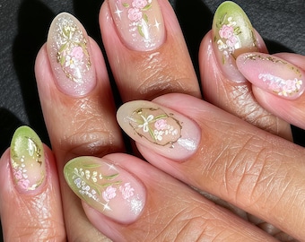 Uña personalizada, efecto degradado rosa-verde con flor pintada a mano y marco dorado, temática natural y serena, ideal para ceremonias nupciales al aire libre.