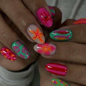 Puede incluir: Uñas de forma ovalada con una manicura vibrante que presenta diversos diseños, incluyendo un cangrejo rojo sobre base rosa, una estrella de mar naranja sobre base nude, peces verdes sobre base turquesa, una flor rosa y varios patrones coloridos.