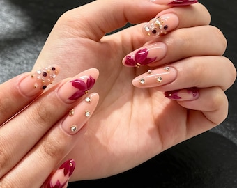 Uñas postizas personalizadas de color morado intenso con diseño floral, pedrería 3D y detalles dorados. Elegantes uñas postizas románticas para bodas o citas románticas.