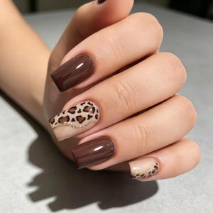 Puede incluir: Uñas manicuradas que presentan una combinación de esmalte marrón oscuro sólido y una base nude con un patrón de leopardo en negro y marrón. Una fina línea de purpurina dorada separa el estampado de leopardo de la base nude en dos uñas.